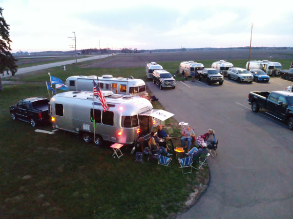 Silver Airstream trailers at dusk with a campfire circle and acoustic guitar.