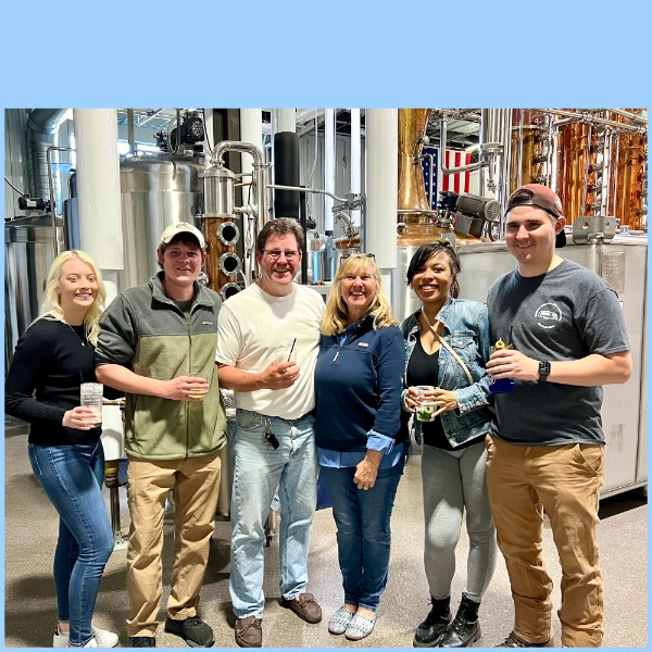 Friends with cocktails in front of copper stills at Rush Creek Distilling.
