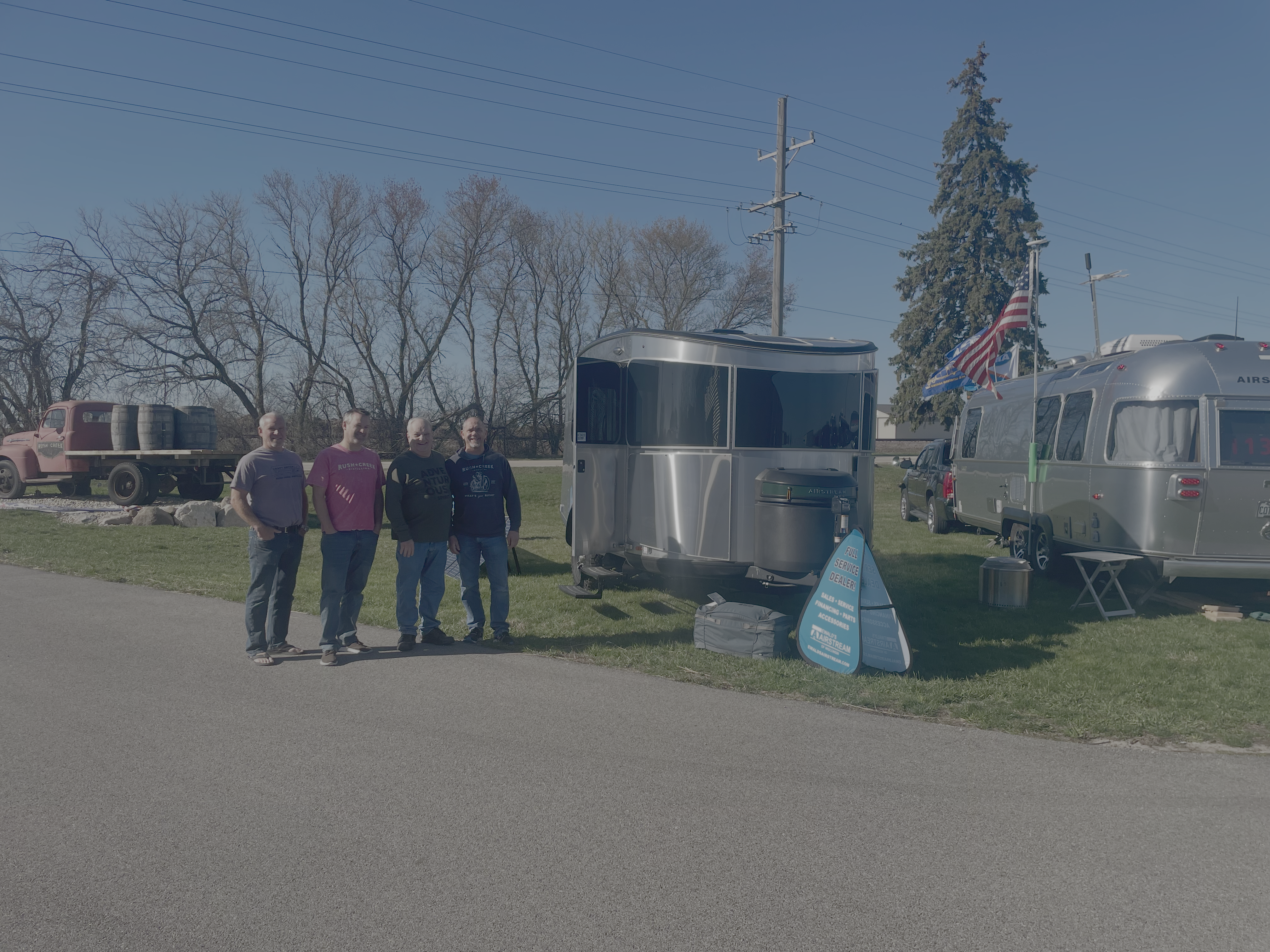 Two Airstream trailers on grass beside Rush Creek Distilling with a vintage barrel truck.
